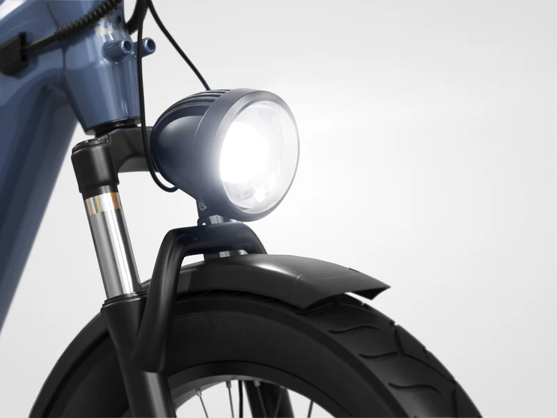 Close-up of a bicycle’s front tire, suspension fork, and illuminated headlight against a plain background.
