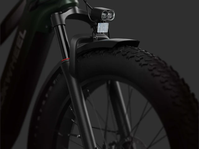 Close-up view of a bicycle’s front tire, fork, and fender, featuring a mounted headlight and reflector against a dark background.