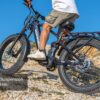 A person rides the Onyx Ebike, a black electric mountain bike with fat tires, up a rocky incline, highlighting its advanced full suspension system.