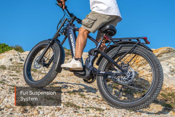A person rides the Onyx Ebike, a black electric mountain bike with fat tires, up a rocky incline, highlighting its advanced full suspension system.