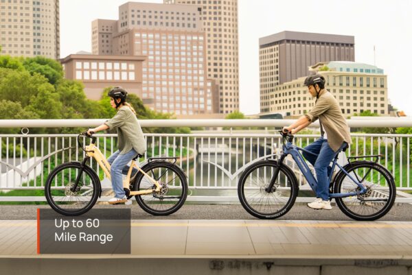 Two riders in helmets cross a city bridge on Tarmac Ebikes, with skyscrapers behind them. Text overlay: "Tarmac Ebike – Up to 60 Mile Range.