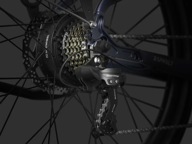 Close-up view of a bicycle rear derailleur and gear cassette, showing the Shimano Tourney mechanism and multiple sprockets.