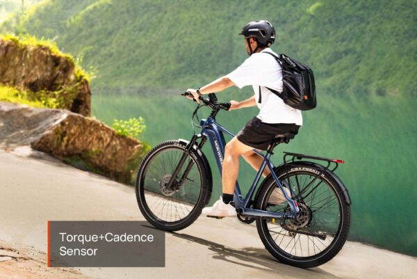 A person wearing a helmet and backpack rides the Tarmac ST Ebike downhill near a lake, with text overlay: "Torque+Cadence Sensor".