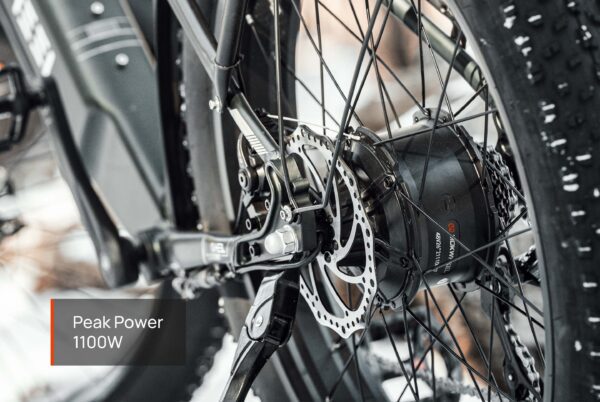 Close-up of the Tor Plus Ebike’s rear wheel showing its disc brake and motor, with a label displaying “Peak Power 1100W.”.