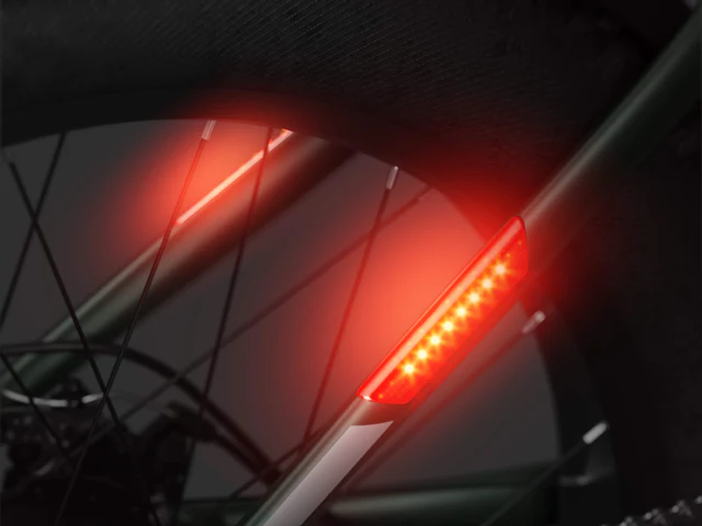 Close-up of a bicycle rear wheel with a red LED light attached to the frame, glowing brightly for visibility.