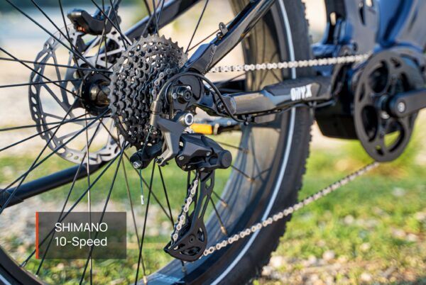 Close-up of the Onyx Ebike's rear wheel featuring a Shimano 10-speed derailleur, cassette, chain, and part of the frame on a grassy surface.