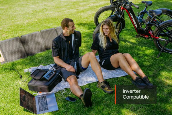 A man and woman relax on a blanket near Obsidian ST Ebikes, using solar panels to charge devices. Text on image: "Inverter Compatible".