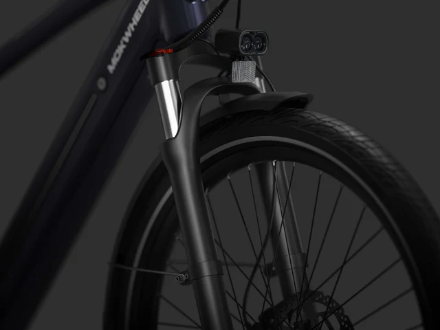 Close-up of a bicycle front fork, tire, and headlight, with visible cables and part of the bike frame against a dark background.