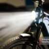 Close-up of the Tarmac Ebike's front fork and tire, featuring a bright integrated headlight turned on, with the label "Integrated Headlight" in the lower right corner.