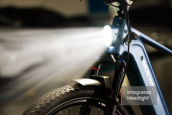 Close-up of the Tarmac Ebike's front fork and tire, featuring a bright integrated headlight turned on, with the label "Integrated Headlight" in the lower right corner.