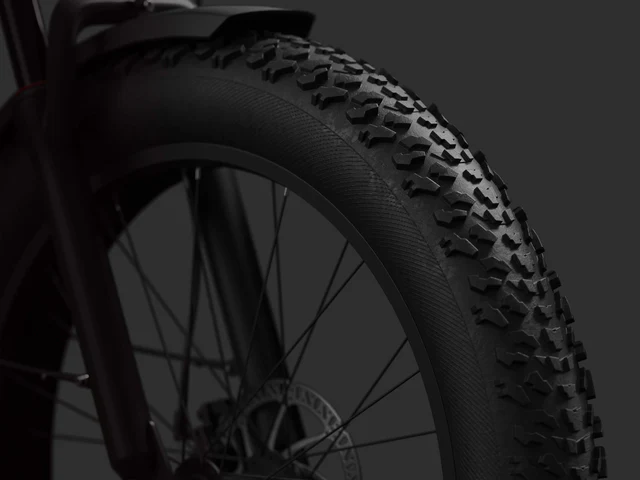 Close-up of a black mountain bike tire with thick, knobby tread and spokes visible against a dark background.