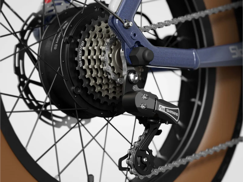 Close-up of a bicycle rear wheel showing the Shimano derailleur, gear cassette, chain, and spokes on a blue bike frame.