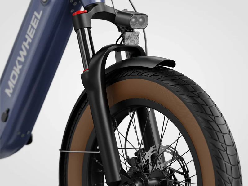 Close-up of the front wheel and suspension fork of a Mokwheel bicycle, featuring a brown tire, disc brake, and mounted front light.