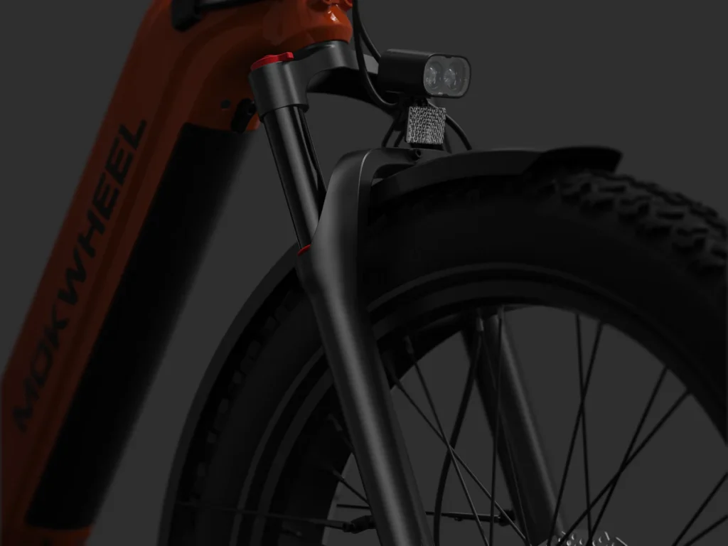 Close-up view of the front wheel, fork, headlight, and fender of an orange Mokwheel electric bicycle against a dark background.