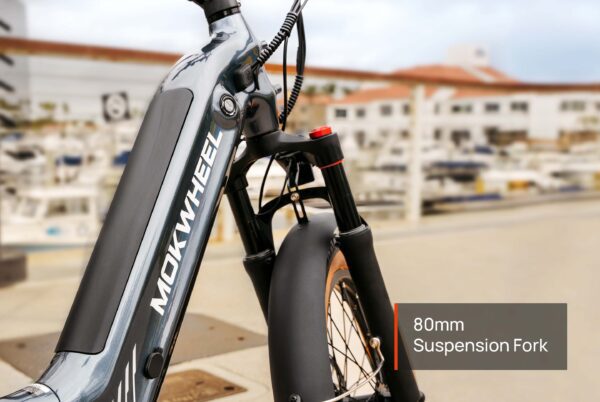 Close-up of the front section of a Slate Ebike, showcasing its 80mm suspension fork, with a marina and buildings softly blurred in the background.