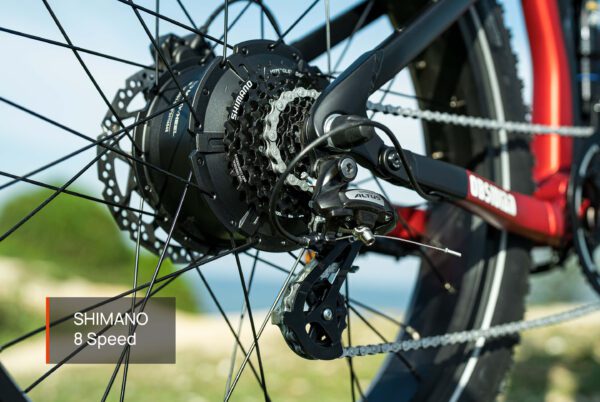 Close-up of the Obsidian ST Ebike's rear wheel featuring the Shimano 8-speed gear system, chain, cassette, and derailleur, set against a blurred outdoor background.