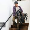 A person wearing a helmet carries a folded Slate Ebike with 3'' fat tires down stairs. Text overlay: "Foldable-3'' Fat Tire.