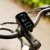 Close-up of the Tarmac Ebike handlebar featuring a digital display showing speed, battery level, and settings, with a blurred outdoor background.