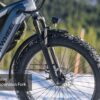 Close-up of the Tor Plus Ebike’s front wheel, featuring a suspension fork marked 110mm, with snowy terrain and trees visible in the background.