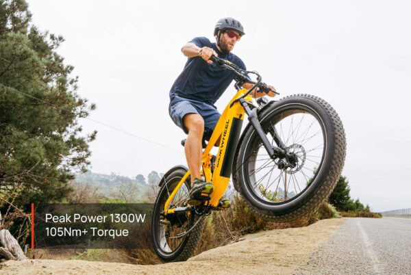 A man rides the Obsidian ST Ebike, a yellow electric bike, up a dirt incline with the front wheel lifted. Text on image: "Peak Power 1300W, 105Nm+ Torque.