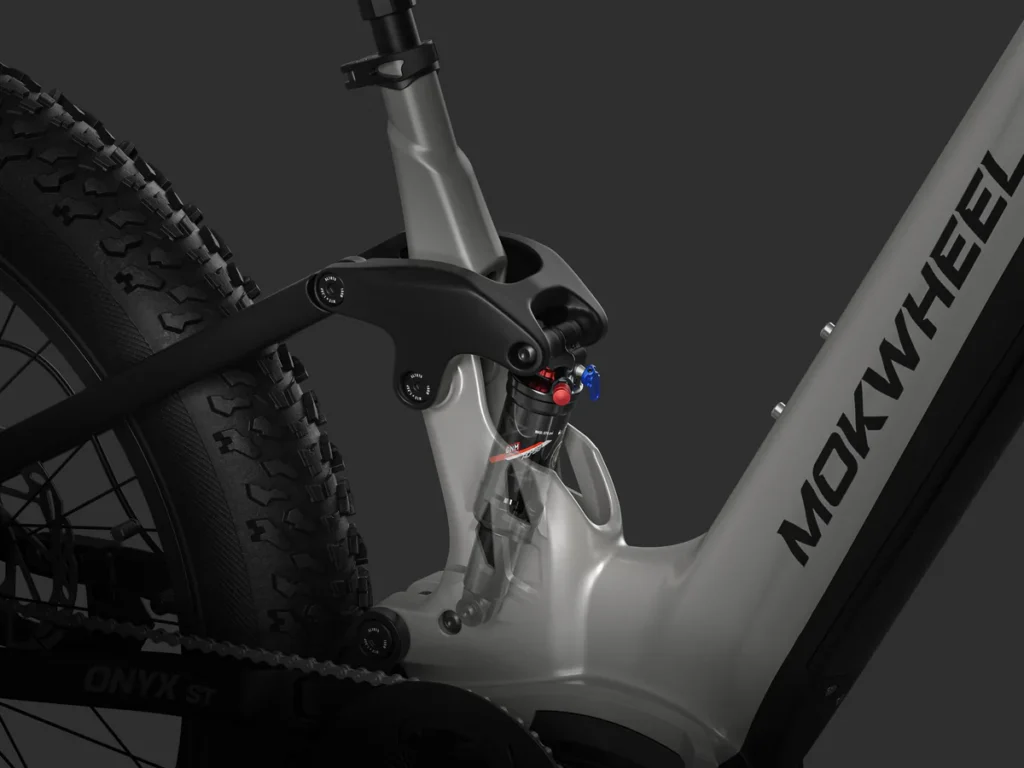 Close-up of the rear suspension system on a MOKWHEEL electric bike, showing the shock absorber, frame, and part of the rear tire against a dark background.