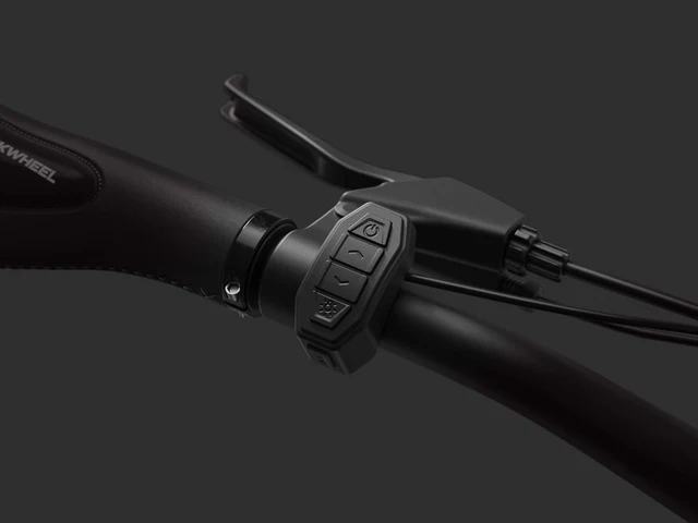 Close-up of a bicycle handlebar featuring a control module with buttons and a brake lever against a dark background.