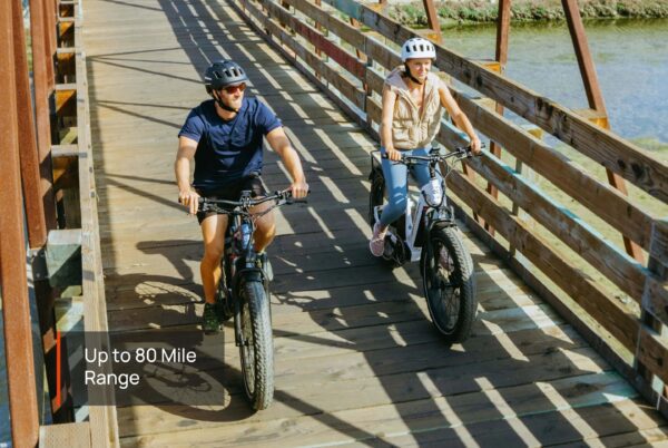 Two people wearing helmets ride Basalt Ebikes across a wooden bridge over water. Text on image reads, "Up to 80 Mile Range.