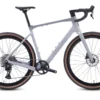 A matte gray gravel bike with drop handlebars, disc brakes, and wide tan-wall tires is shown in a side view against a white background.