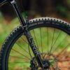 Close-up of a mountain bike's front suspension fork, wheel, and tire with "RockShox" and "Union DHF" visible, set against a blurred natural background.