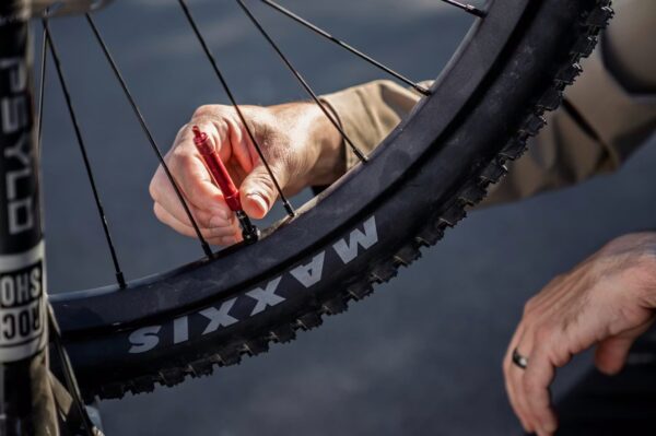 A person uses a red tool to check or adjust the tire valve of a mountain bike with Maxxis tires.