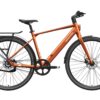Orange Mokwheel electric commuter bike with a rear rack, fenders, and belt drive.