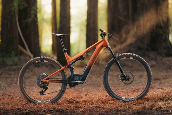 Orange and black Aventon electric mountain bike parked on a forest floor.